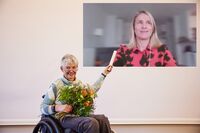 Sigrid Arnade mit Blumenstrauß im Rollstuhl sitzend überreicht Verena Bentele (online zugeschaltet) den DBR-Staffelstab; beide lächeln