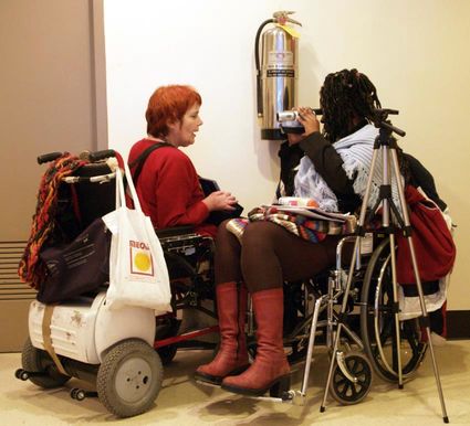 Dinah Radtke, sitting in her power wheelchair contacting a black woman using a wheelchair